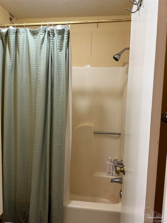 bathroom with a textured ceiling and shower / tub combo with curtain