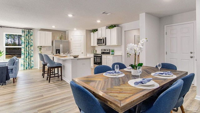 dining room featuring light wood-type flooring, visible vents, recessed lighting, and a textured ceiling