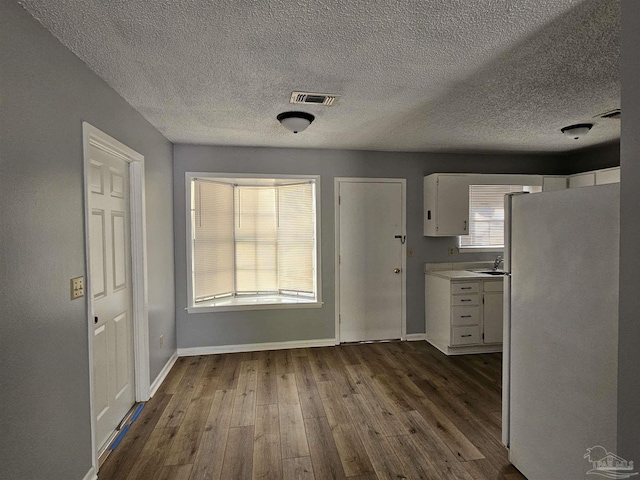 kitchen featuring white refrigerator, dark hardwood / wood-style flooring, a textured ceiling, and white cabinets