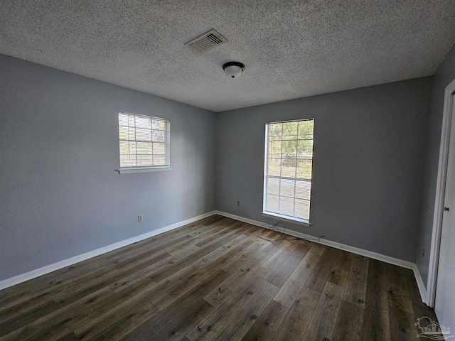 empty room with dark hardwood / wood-style floors, a wealth of natural light, and a textured ceiling