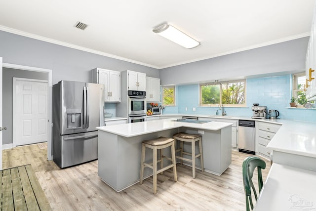 kitchen with a sink, a center island, light wood-type flooring, stainless steel appliances, and visible vents