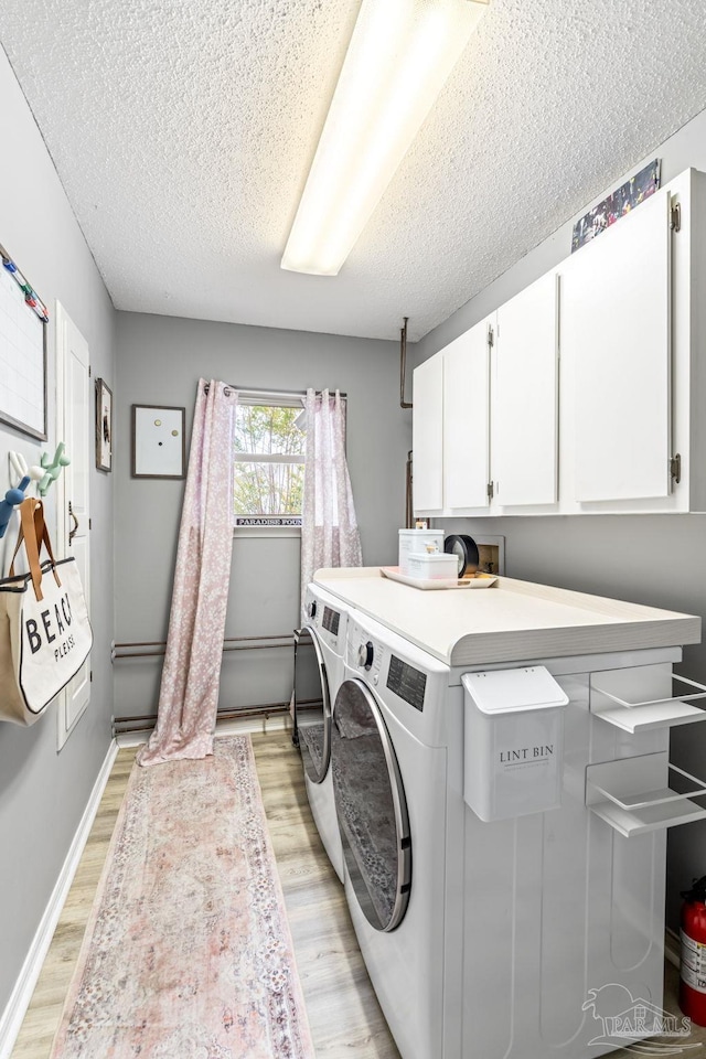 clothes washing area featuring a textured ceiling, baseboards, light wood-type flooring, washer and dryer, and cabinet space