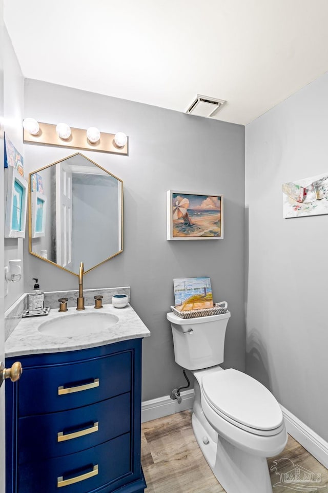 half bathroom with vanity, toilet, baseboards, visible vents, and wood finished floors