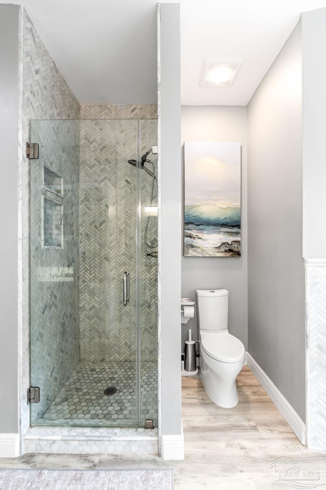 bathroom featuring a shower stall, baseboards, wood finished floors, and toilet
