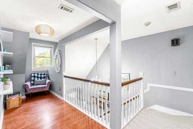 hall featuring baseboards, visible vents, an upstairs landing, and wood finished floors