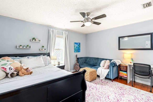 bedroom featuring baseboards, a textured ceiling, visible vents, a ceiling fan, and wood finished floors