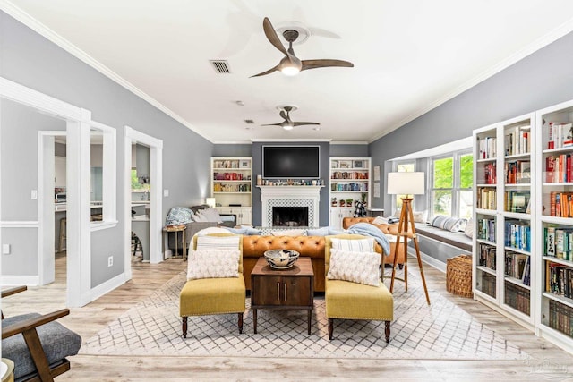 interior space with a tiled fireplace, wood finished floors, visible vents, ceiling fan, and ornamental molding