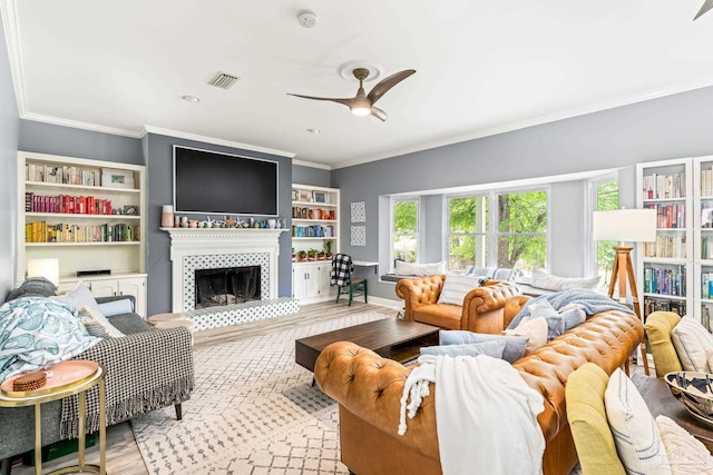 living room with ornamental molding, visible vents, a tiled fireplace, a ceiling fan, and wood finished floors