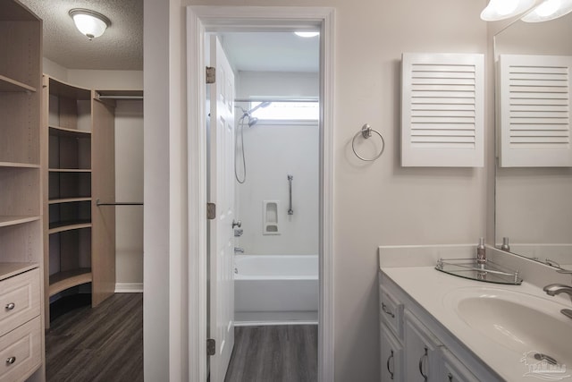 bathroom with a textured ceiling, shower / bath combination, wood finished floors, and vanity