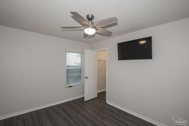 unfurnished bedroom featuring baseboards, dark wood-style floors, ceiling fan, a spacious closet, and a textured ceiling