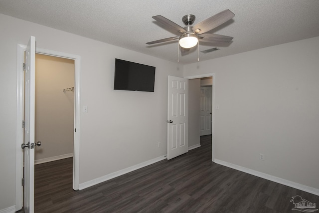 unfurnished bedroom with a textured ceiling, a spacious closet, and dark wood finished floors