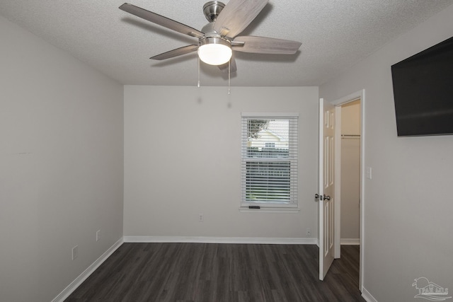 unfurnished bedroom featuring a textured ceiling, dark wood-style flooring, baseboards, a closet, and a walk in closet