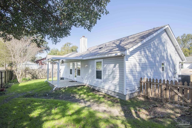 rear view of house featuring central AC unit, a fenced backyard, a chimney, a yard, and a patio area