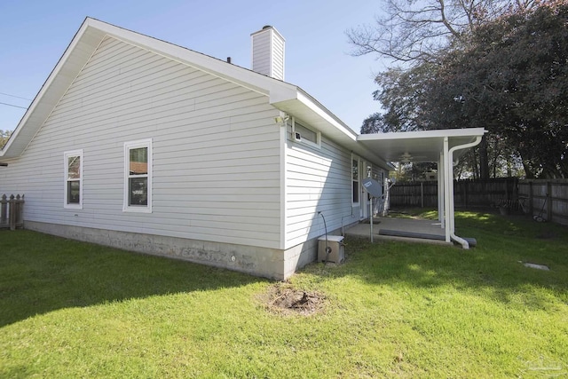 view of side of home with a lawn, a chimney, and fence