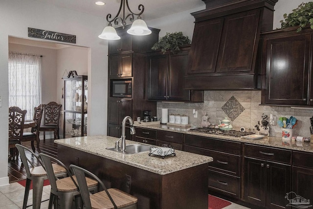 kitchen featuring sink, decorative backsplash, stainless steel gas stovetop, and a center island with sink