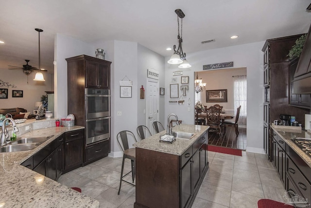 kitchen with pendant lighting, sink, a breakfast bar area, stainless steel double oven, and a center island with sink