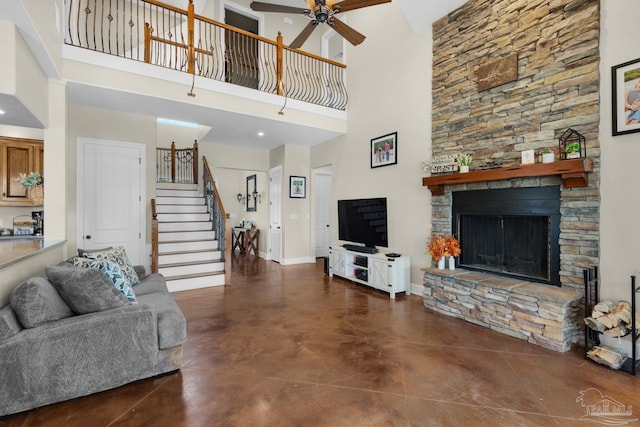 living room with a stone fireplace, a towering ceiling, and ceiling fan