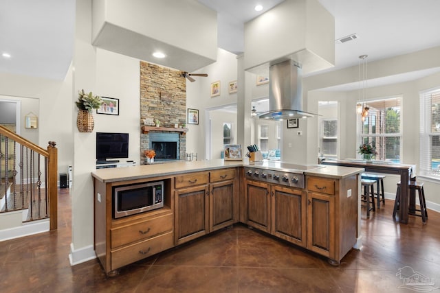 kitchen with kitchen peninsula, island exhaust hood, a fireplace, decorative light fixtures, and stainless steel appliances