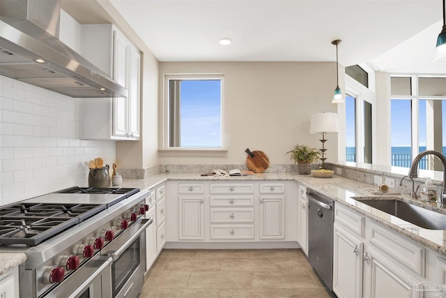 kitchen featuring stainless steel appliances, sink, wall chimney range hood, and decorative light fixtures