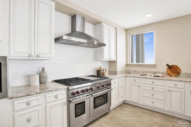 kitchen featuring white cabinetry, backsplash, range with two ovens, light stone counters, and wall chimney exhaust hood