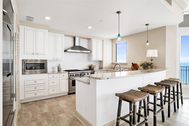 kitchen with white cabinetry, wall chimney exhaust hood, stainless steel appliances, and light stone countertops