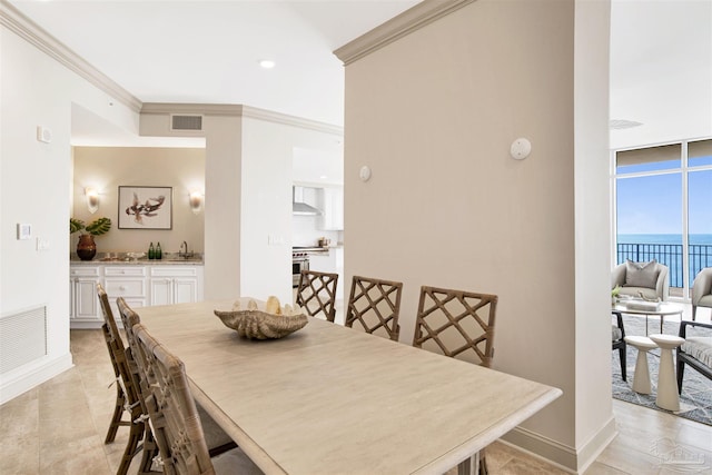 dining room with a water view, a wall of windows, crown molding, and sink