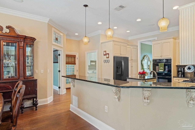 kitchen with light wood-type flooring, hanging light fixtures, black appliances, and cream cabinetry