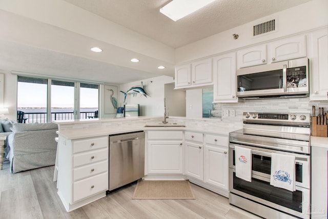 kitchen with visible vents, appliances with stainless steel finishes, open floor plan, a peninsula, and backsplash