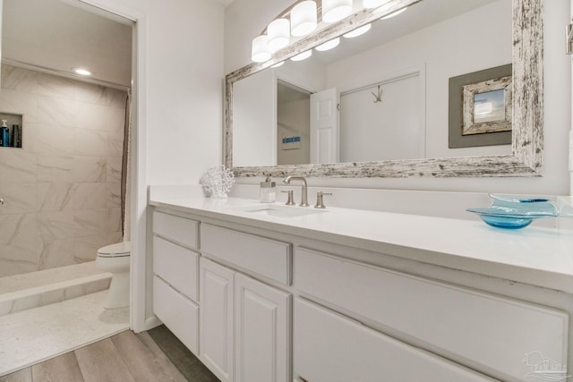 bathroom with a tile shower, vanity, toilet, and wood finished floors