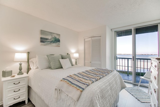 bedroom featuring dark wood-style floors, a water view, access to outside, a textured ceiling, and a closet