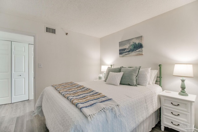 bedroom with a closet, visible vents, a textured ceiling, and wood finished floors