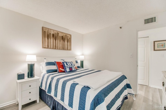 bedroom featuring light wood finished floors, baseboards, visible vents, and a textured ceiling