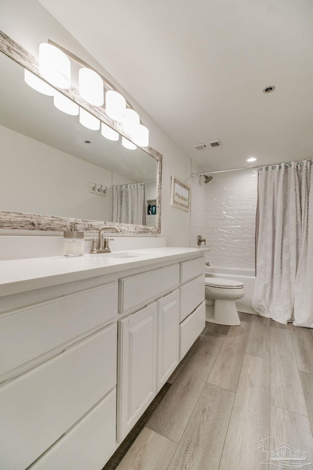 bathroom featuring visible vents, toilet, wood finished floors, shower / bathtub combination with curtain, and vanity