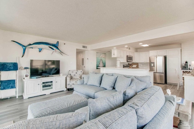 living room featuring light wood-style flooring, visible vents, and a textured ceiling