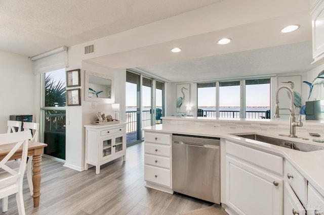 kitchen with light wood finished floors, visible vents, white cabinets, stainless steel dishwasher, and a sink