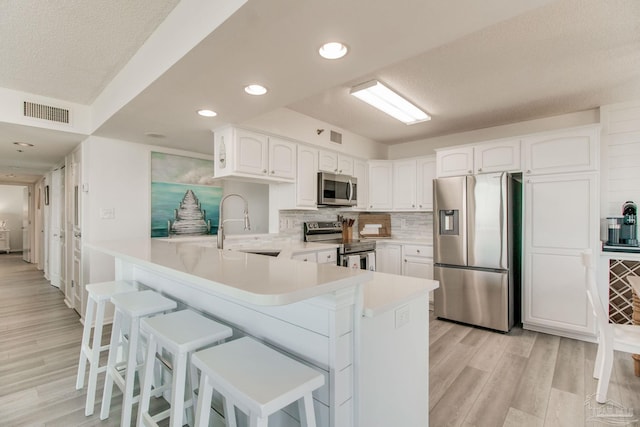 kitchen with stainless steel appliances, a breakfast bar, a peninsula, visible vents, and light wood-type flooring