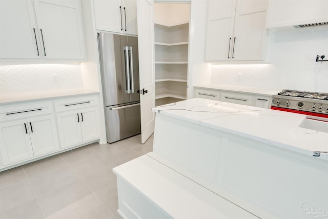 kitchen with light tile patterned floors, backsplash, high end fridge, light stone countertops, and custom exhaust hood