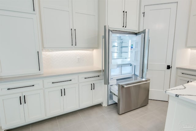 kitchen featuring tasteful backsplash, stainless steel refrigerator, light tile patterned floors, white cabinets, and light stone counters