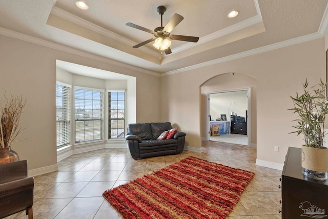 living room featuring a textured ceiling, a raised ceiling, light tile patterned floors, ornamental molding, and ceiling fan