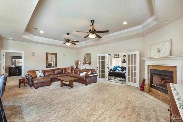 living room with ceiling fan, a tray ceiling, a tiled fireplace, and french doors