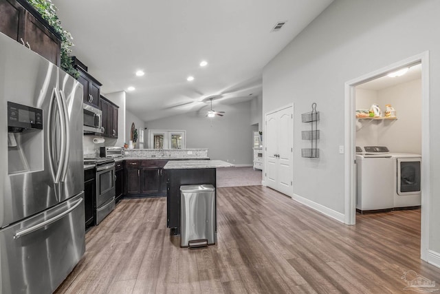 kitchen with vaulted ceiling, appliances with stainless steel finishes, a kitchen breakfast bar, a kitchen island, and washing machine and dryer