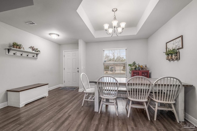 dining room with dark wood-type flooring, a tray ceiling, and a chandelier