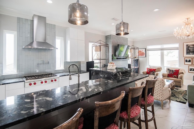 kitchen with dark stone countertops, white cabinets, pendant lighting, and wall chimney range hood