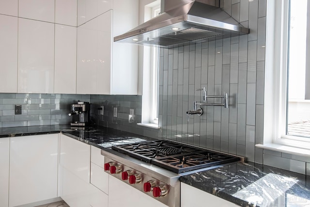 kitchen with stainless steel gas stovetop, wall chimney exhaust hood, dark stone countertops, and white cabinets