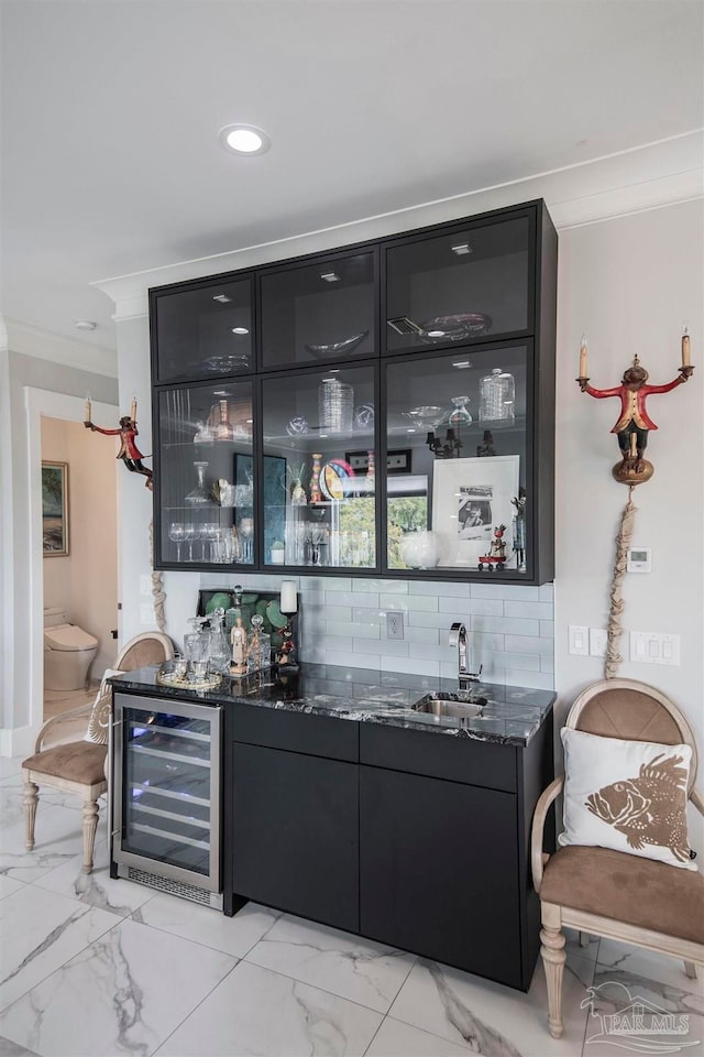 bar featuring dark stone countertops, tasteful backsplash, beverage cooler, ornamental molding, and sink