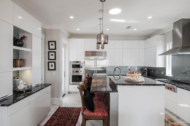 kitchen with white cabinets, a kitchen island, wall chimney exhaust hood, stainless steel appliances, and a kitchen breakfast bar