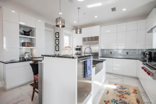 kitchen featuring stainless steel appliances, white cabinetry, a center island with sink, and hanging light fixtures