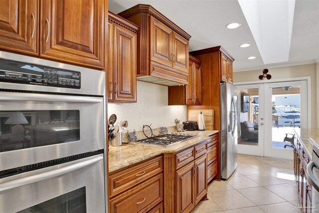 kitchen with appliances with stainless steel finishes, brown cabinets, light stone countertops, french doors, and light tile patterned flooring