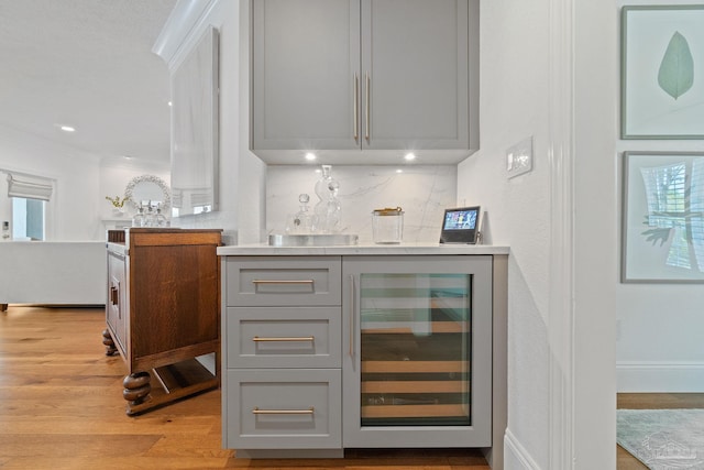 bar with gray cabinetry, a healthy amount of sunlight, ornamental molding, light wood-type flooring, and beverage cooler