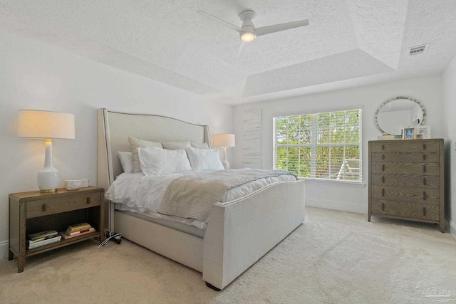 carpeted bedroom with a textured ceiling, a tray ceiling, and ceiling fan